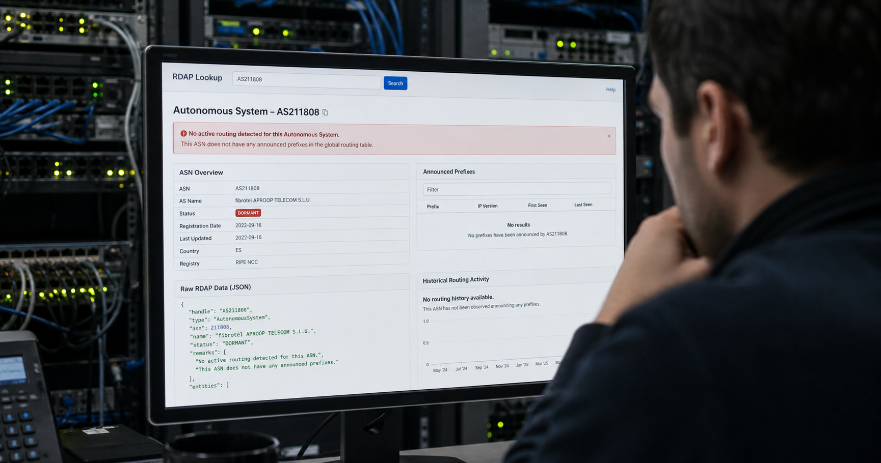 Computer screen showing a RIPE database query result for AS211808 with a 'no announced prefixes' warning, in a dimly lit network operations center with dormant equipment racks.