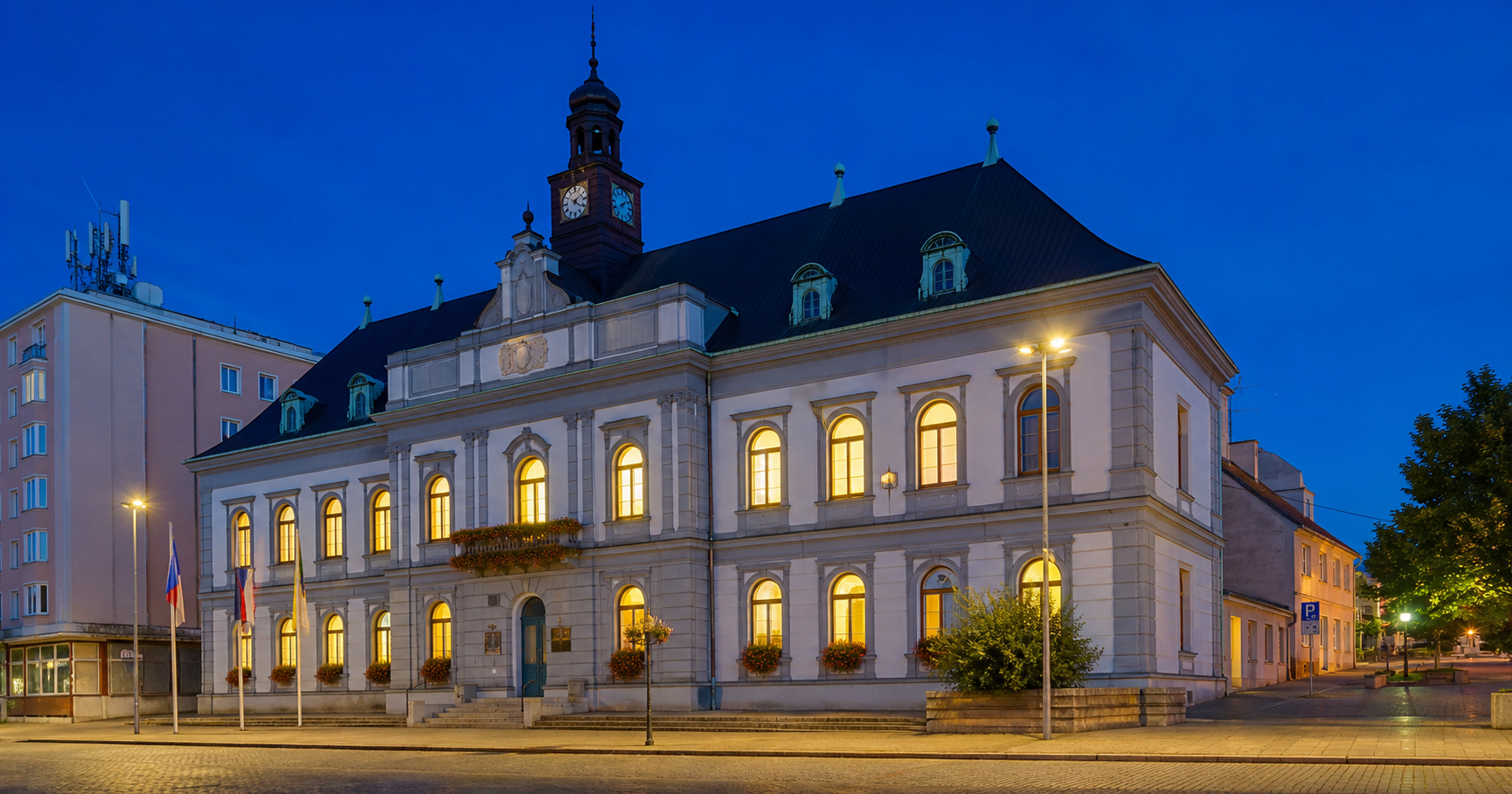 Photograph of the Město Kralupy nad Vltavou municipal building at dusk with lit windows, representing unseen network operations.