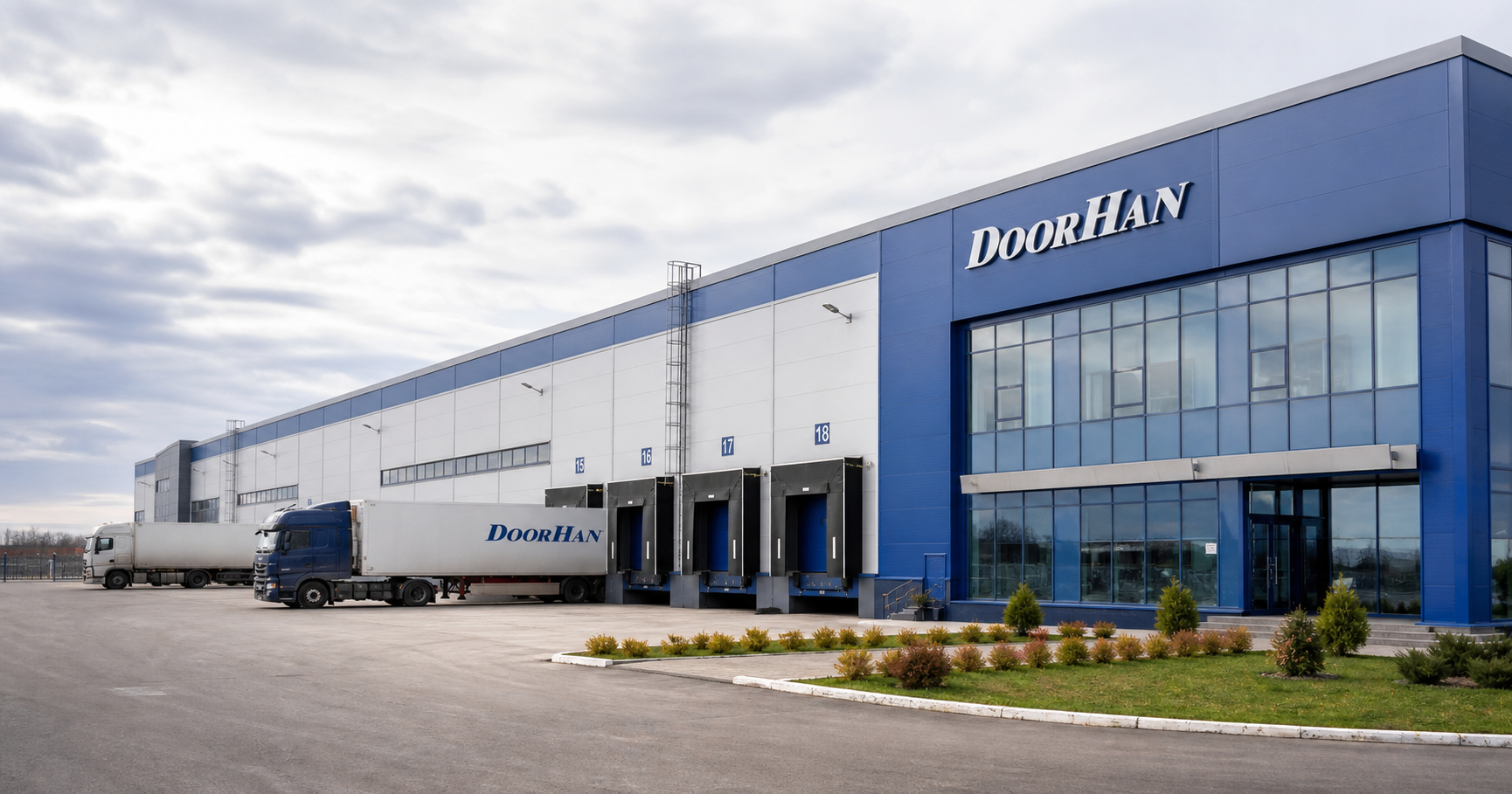A modern industrial building facade with large DoorHan logo, delivery trucks at loading docks, and a partly open industrial gate, under an overcast sky.